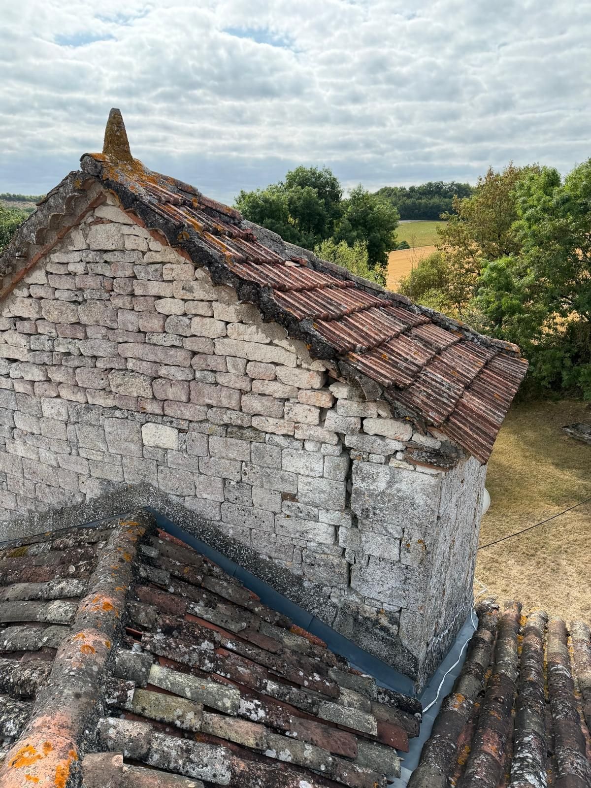 Pignon de pierre et faîtage en tuile canal d'une bâtisse isolée, dans un paysage de coteaux.