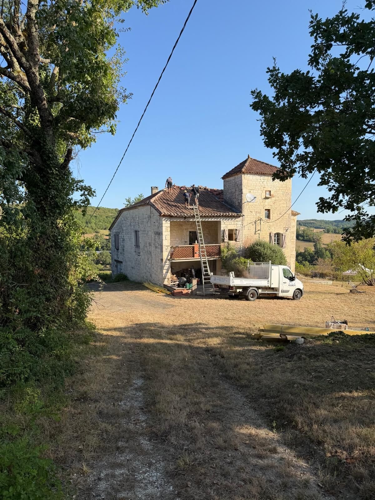 Vue d'ensemble du corps de ferme pendant les travaux, camion benne stationné dans l'allée.