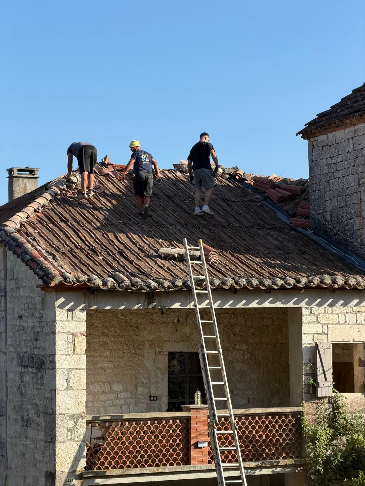 Trois couvreurs sur la toiture pendant la dépose des tuiles, le versant est ouvert sur près de la moitié de sa surface.