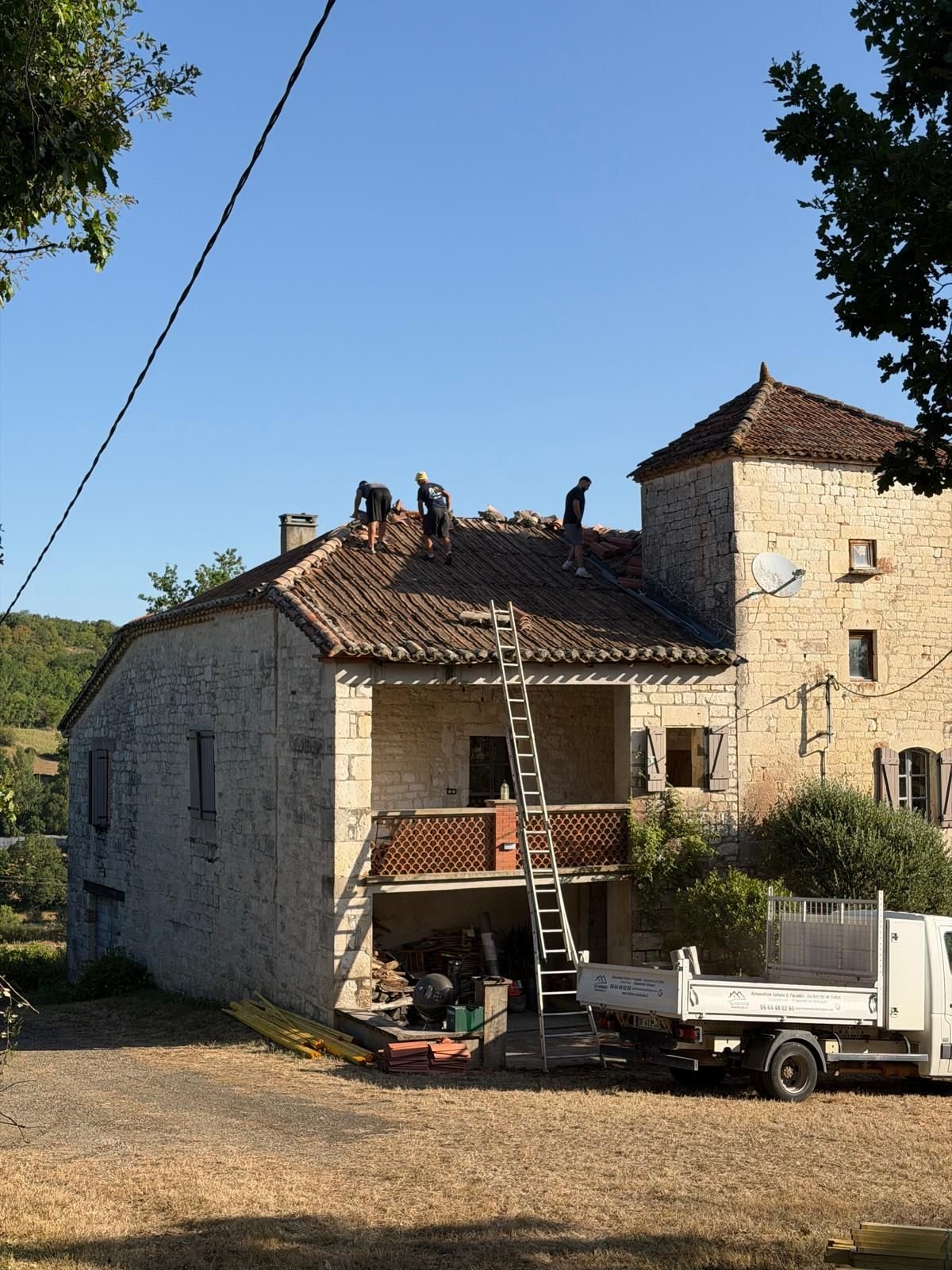 Dépose en cours vue depuis l'extérieur, tuiles retirées et camion benne au pied du bâtiment.