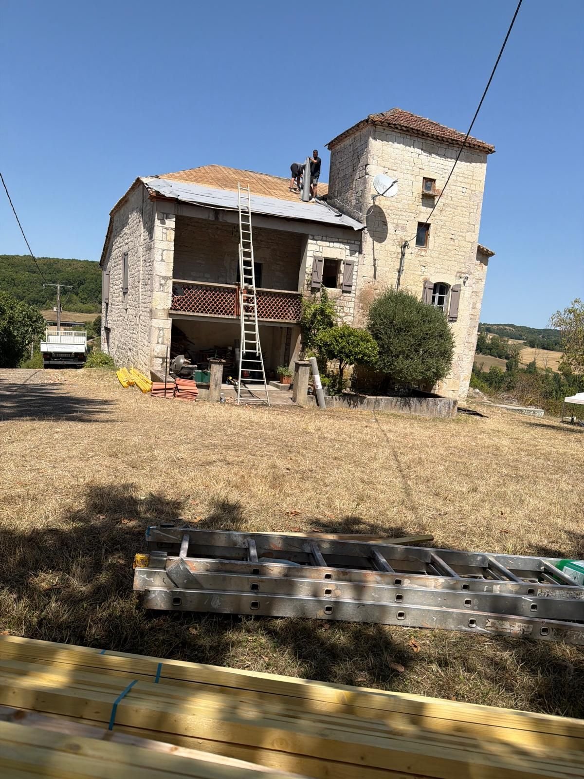 Échelle appuyée contre le pignon, matériel de chantier rangé au sol le long de la façade.