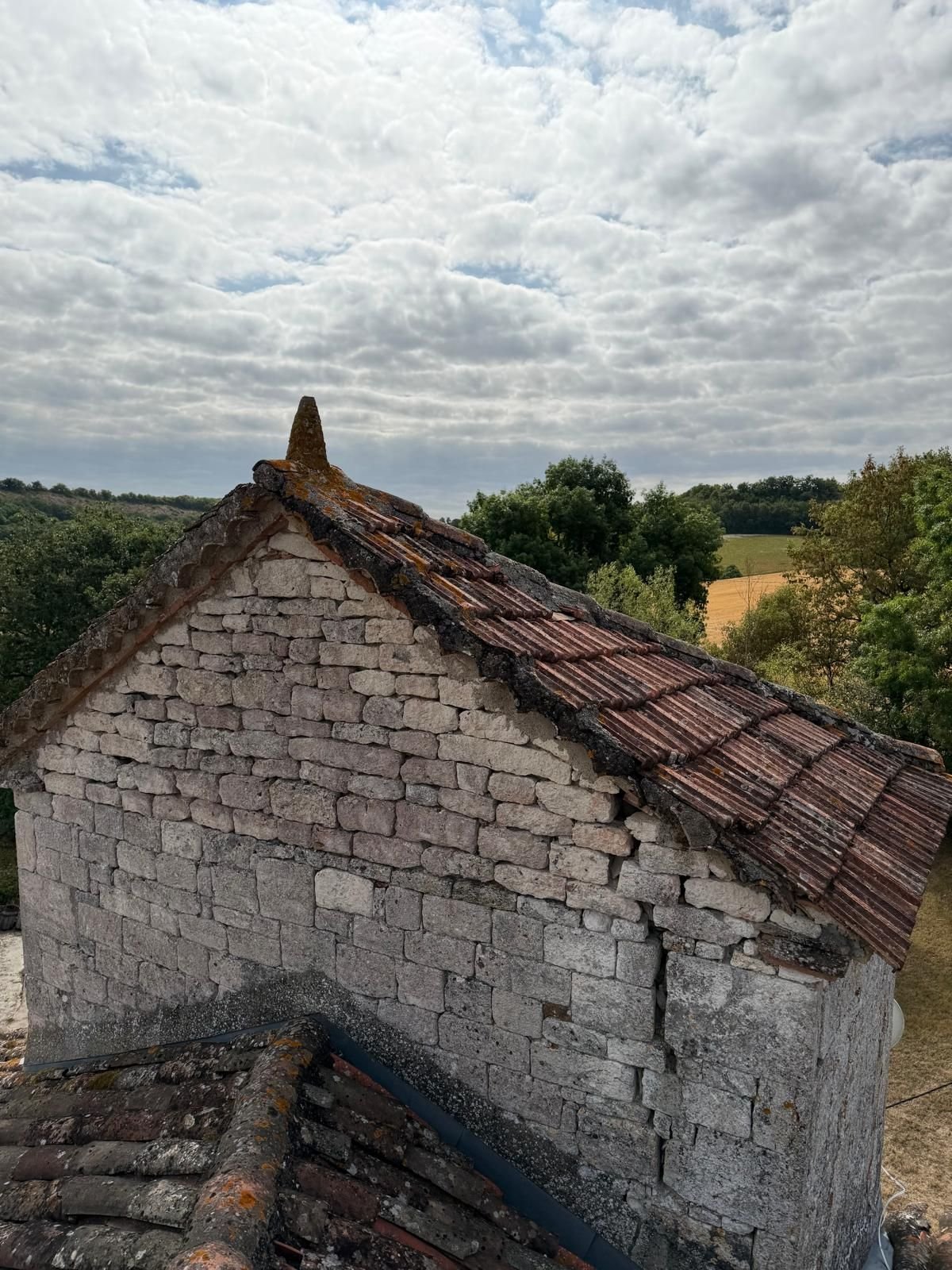 Pignon de pierre et ligne de faîtage de la toiture ancienne, sous un ciel nuageux.