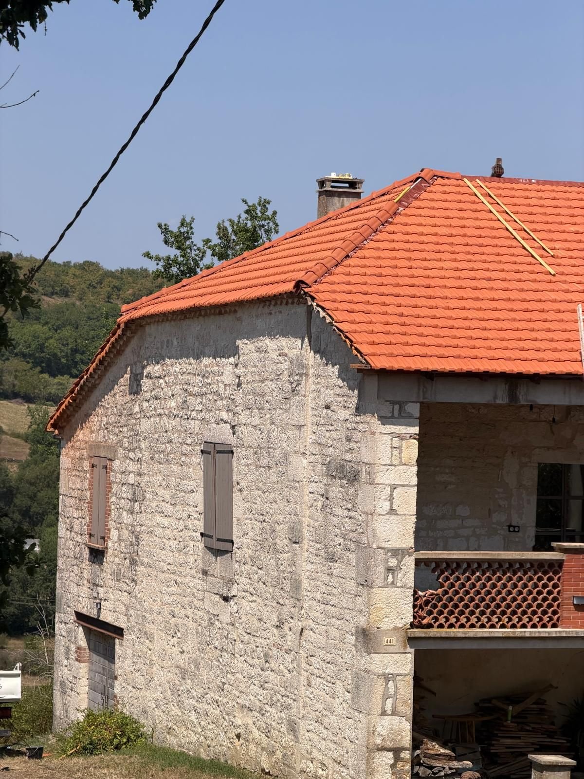 Bâtisse de pierre avec sa couverture neuve en tuile, balcon de bois et volets, vue depuis le pré.