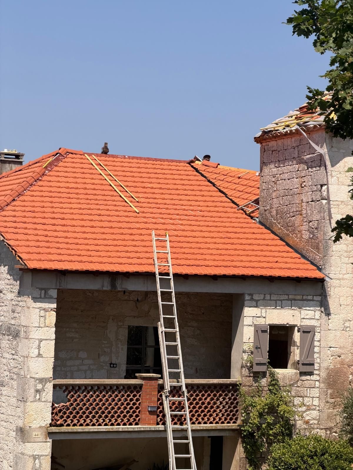 Versant achevé en tuile neuve, échelle posée le long du rampant, souche de cheminée reprise.