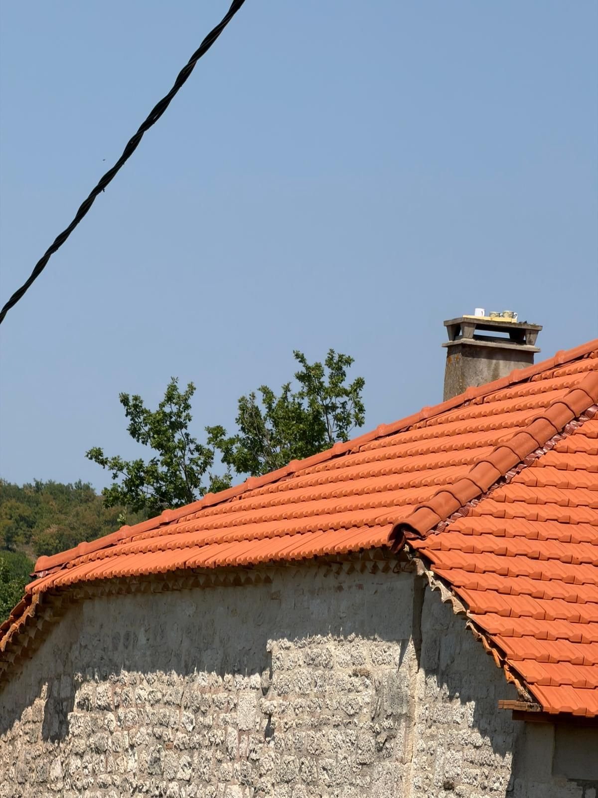 Faîtage neuf d'une dépendance basse et mur de pierre, couverture en tuile refaite.