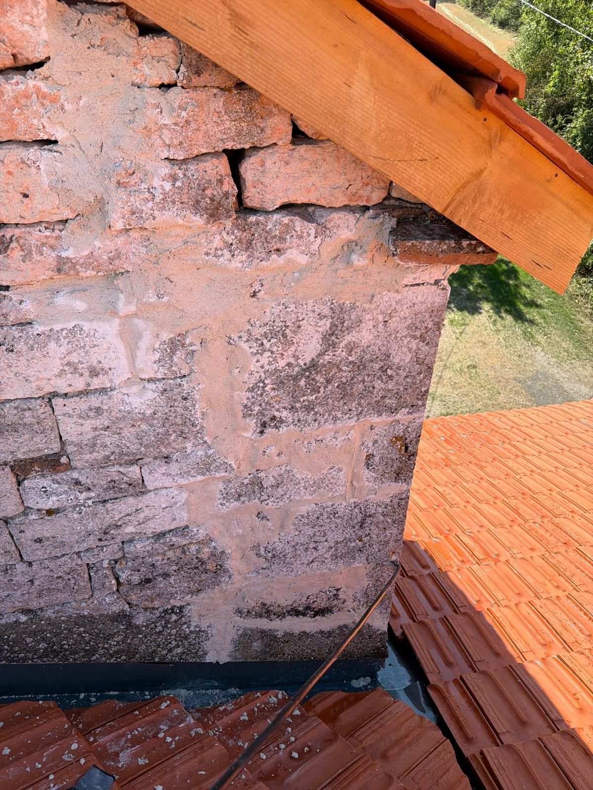 Détail d'un angle de toiture : chevron neuf, premières tuiles reposées et arase du mur de pierre.