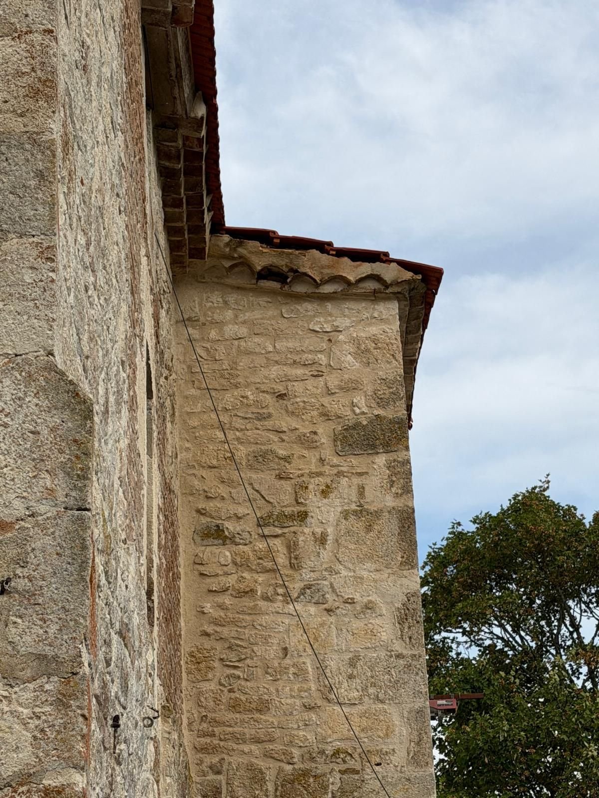 Angle du bâtiment vu en contre-plongée, débord de toit repris au-dessus du mur de pierre.